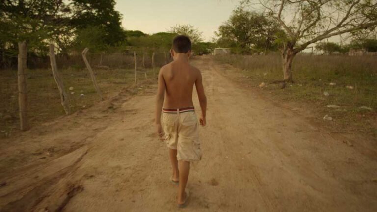 Boy walks barefoot down a dirt road in Artemio.