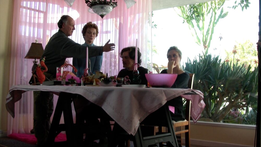 Family at a table with pink curtains, possibly discussing.