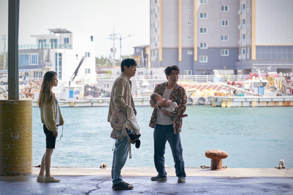 Scene from the film Broker: three adults and a baby stand on a dock.