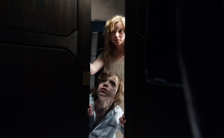 Mother and son peering through a door in "The Babadook," a horror film.