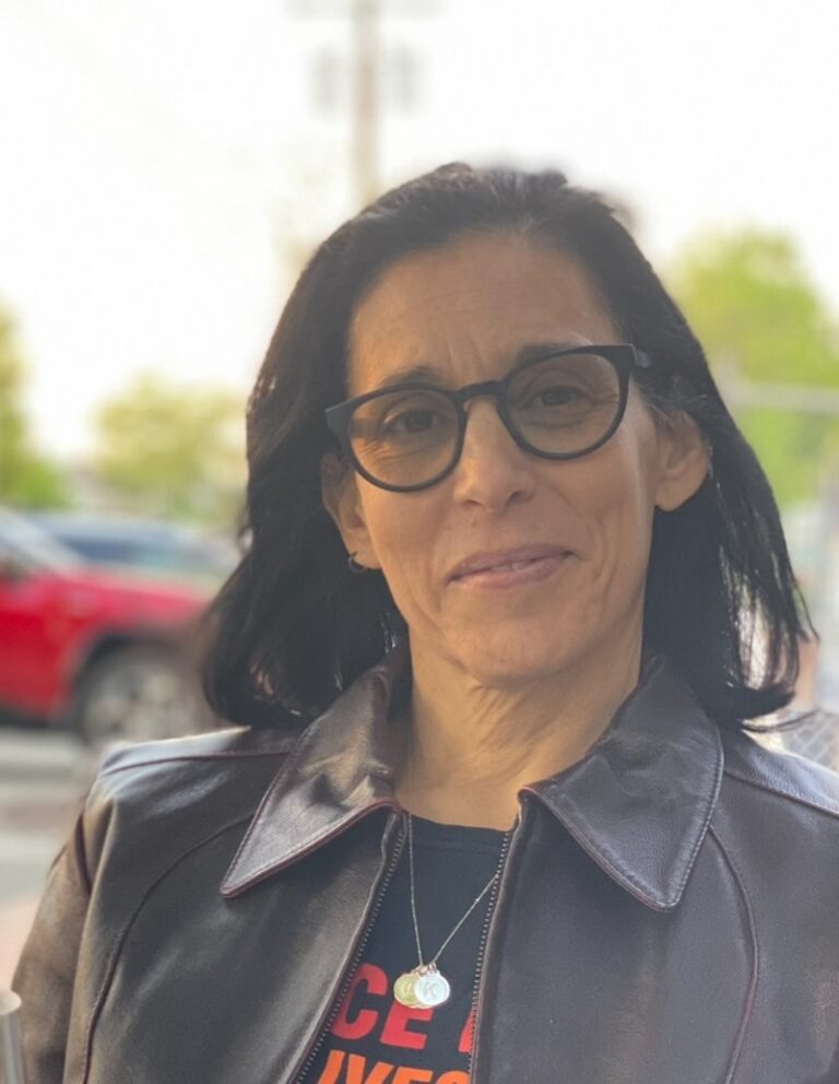 Beatrice Alda wearing glasses and a leather jacket, smiling outdoors.