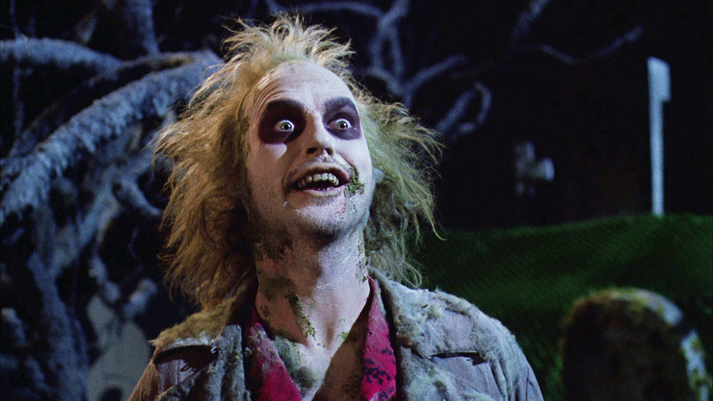 Beetlejuice's wild-eyed expression with messy hair and pale makeup in the movie Beetlejuice.