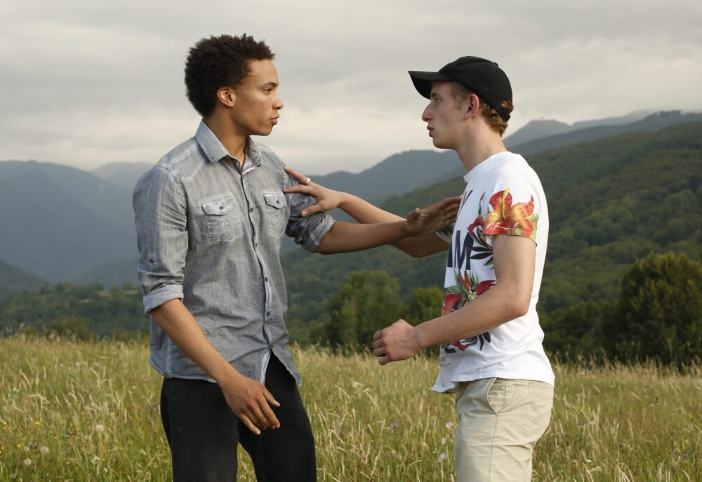 Two young men in a field, one with hand on the other's arm.