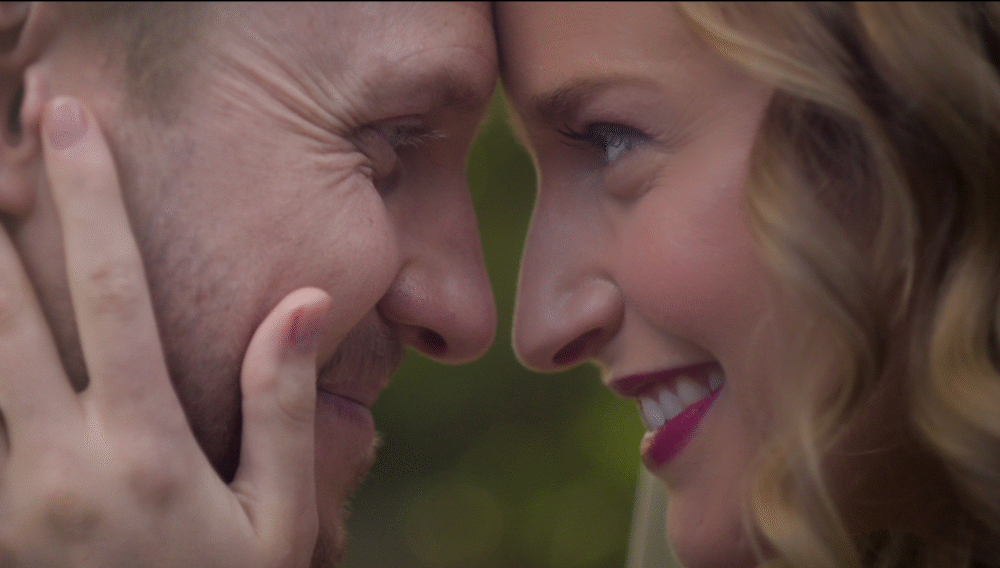 Bernie and Rebecca face-to-face, smiling tenderly with foreheads touching in a close-up portrait of love.