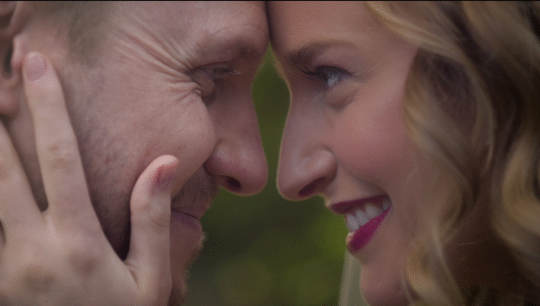 Bernie and Rebecca face-to-face, smiling tenderly with foreheads touching in a close-up portrait of love.