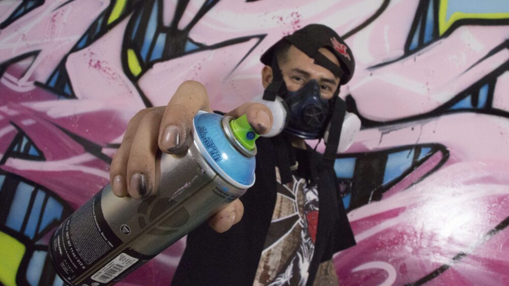 Graffiti artist wearing a respirator and holding a spray paint can.