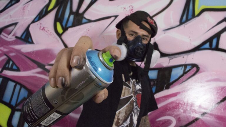 Graffiti artist wearing a respirator and holding a spray paint can.