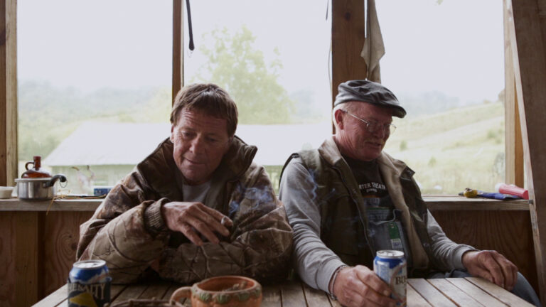 Two men smoking and drinking beer on a porch, rural setting