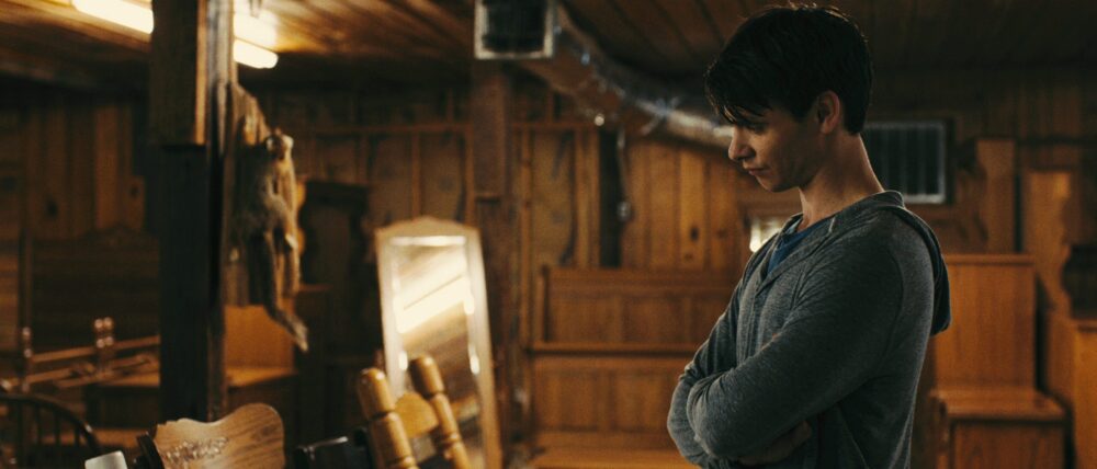 Man with arms crossed in wooden cabin, looking down. Mood shot from Big Significant Things.