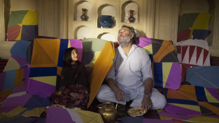 Man and girl surrounded by colorful kites, looking up.