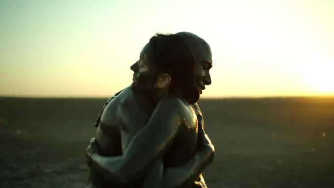 Two people covered in mud hugging on a dark beach at sunset. Black Sea.