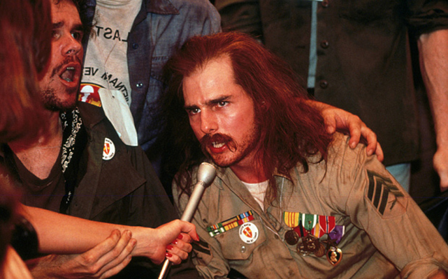 Tom Cruise in "Born on the Fourth of July" as Ron Kovic, speaking into a microphone, wearing military attire.
