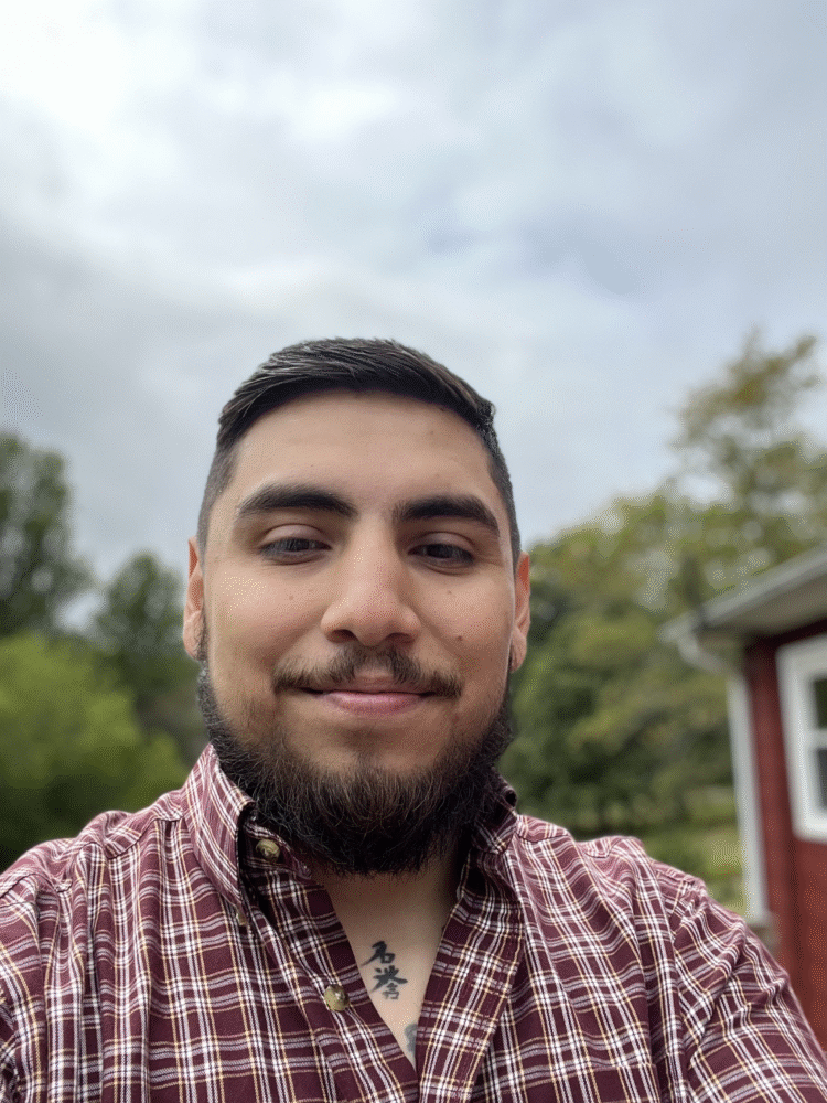 Brayan Florian in a maroon plaid shirt smiles outdoors.