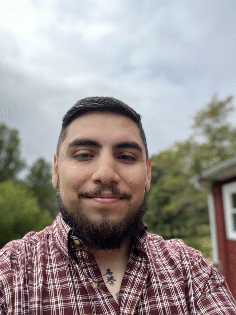 Brayan Florian in a maroon plaid shirt smiles outdoors.