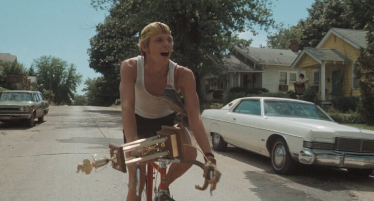 Dennis Christopher celebrates a win in Breaking Away, riding his bike with a trophy.
