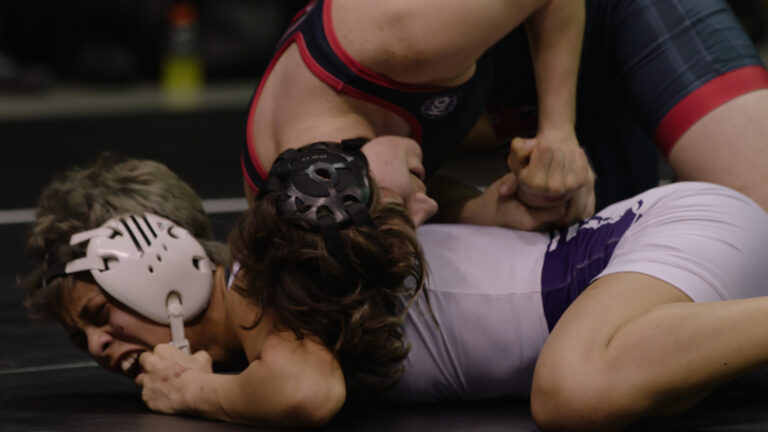 Wrestling match: two wrestlers grappling on the mat during intense competition.