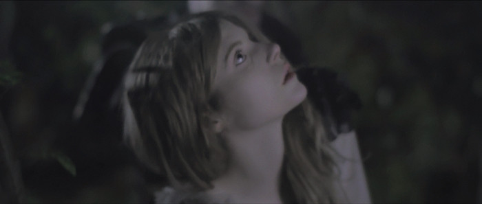 Young woman with blonde hair looking up in a dark, mysterious setting.