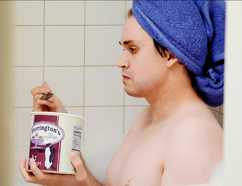 Man with towel eating Ferrington's ice cream in the shower.