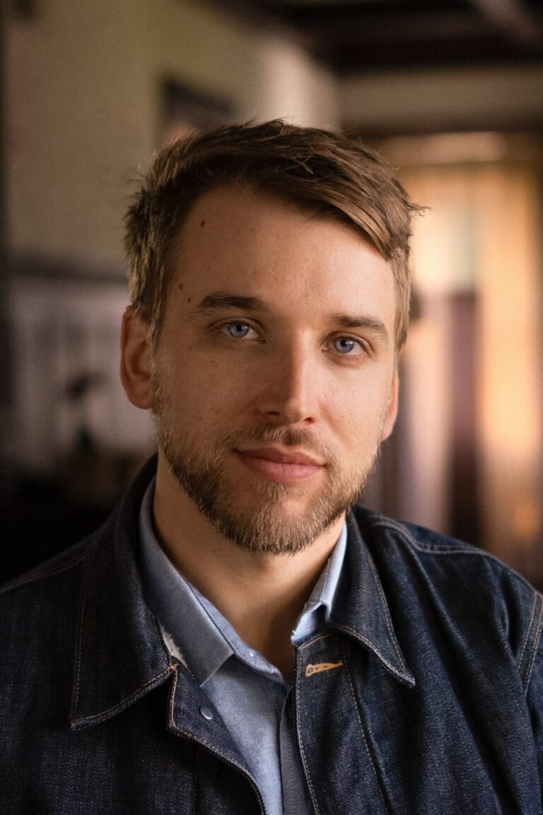 Portrait of Carson Lund with blue eyes, wearing a denim jacket.