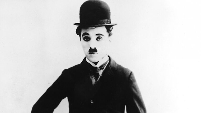 Charlie Chaplin as the Tramp, wearing his iconic bowler hat and mustache.