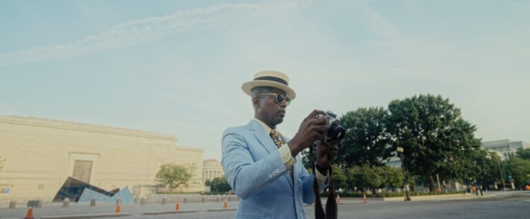 Man in a light blue suit and boater hat takes a photo with a vintage camera in Washington, D.C.