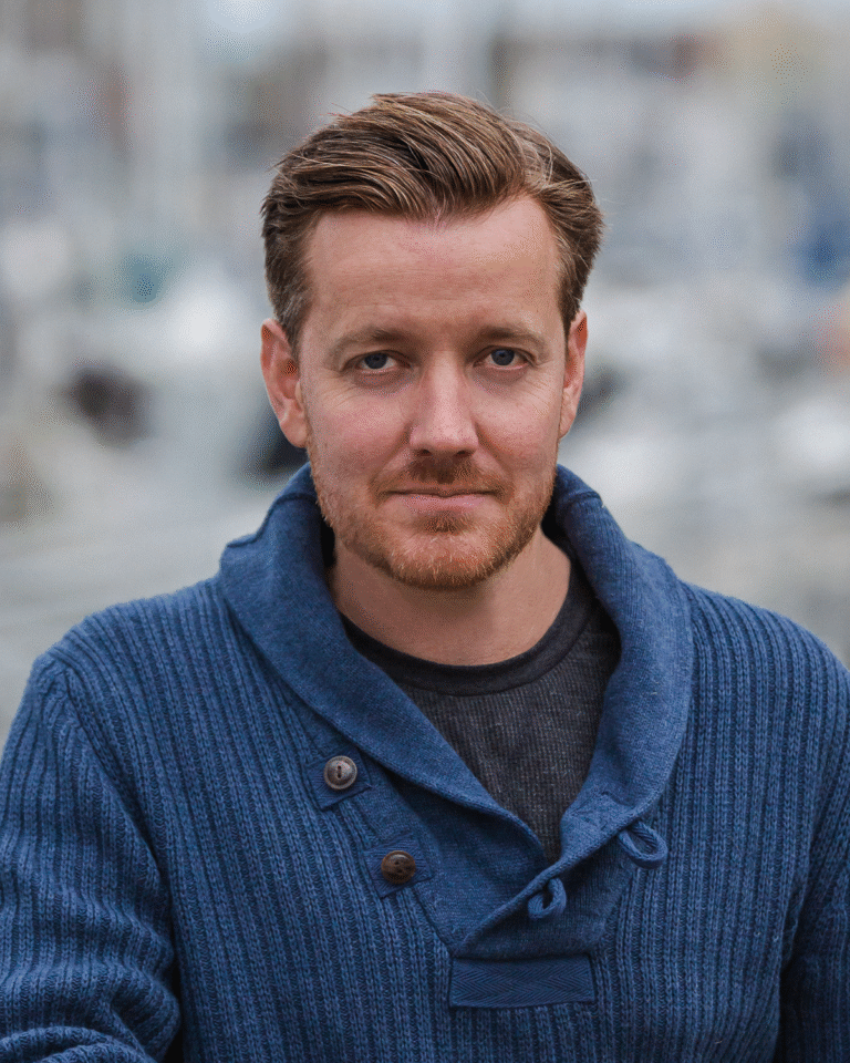 Chris Burke portrait; man with red hair and beard wearing a blue sweater.