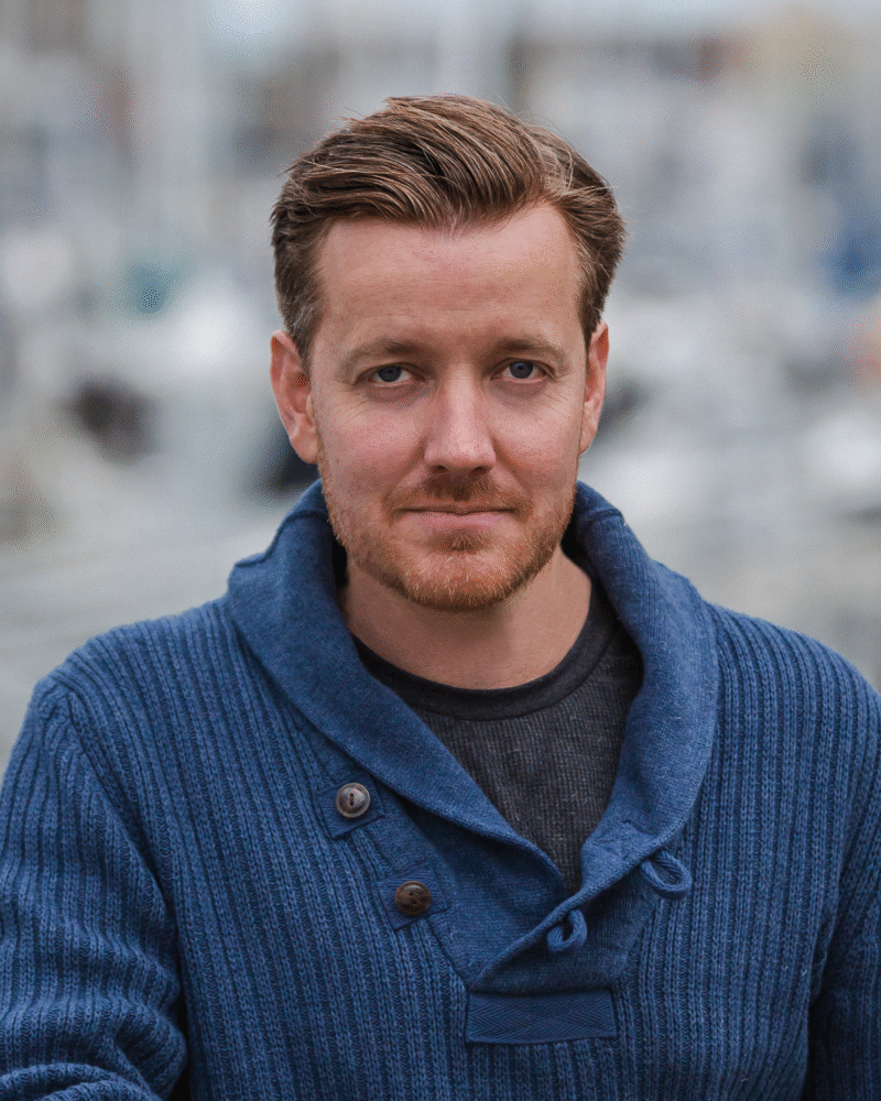 Chris Burke portrait; man with red hair and beard wearing a blue sweater.