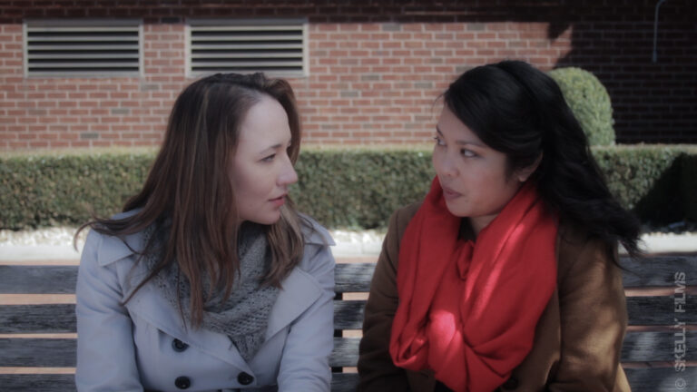 Two women in coats sitting on a bench, engaged in conversation.