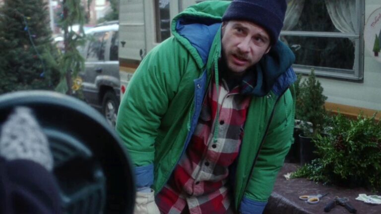 Man in a green jacket and beanie near Christmas trees, possibly from the movie "Christmas, Again".