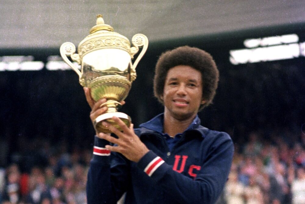 Arthur Ashe holding the Wimbledon trophy, wearing a USA jacket, celebrating his historic win.