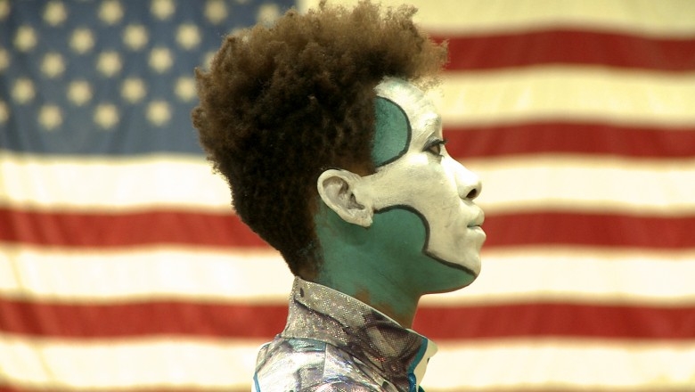 Performer with face paint against an American flag backdrop.