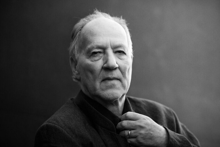 Werner Herzog portrait in black and white, adjusting his collar.