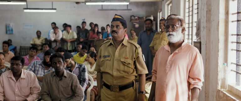 Scene from the film Court, featuring a police officer and an older man with a white beard.