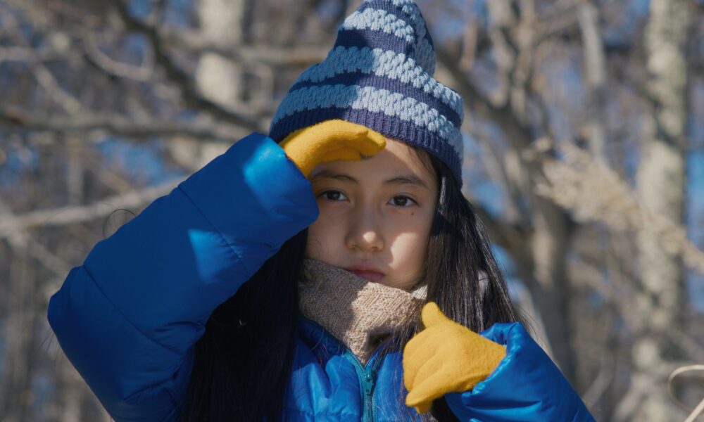 Girl in winter clothes shields her eyes outside.