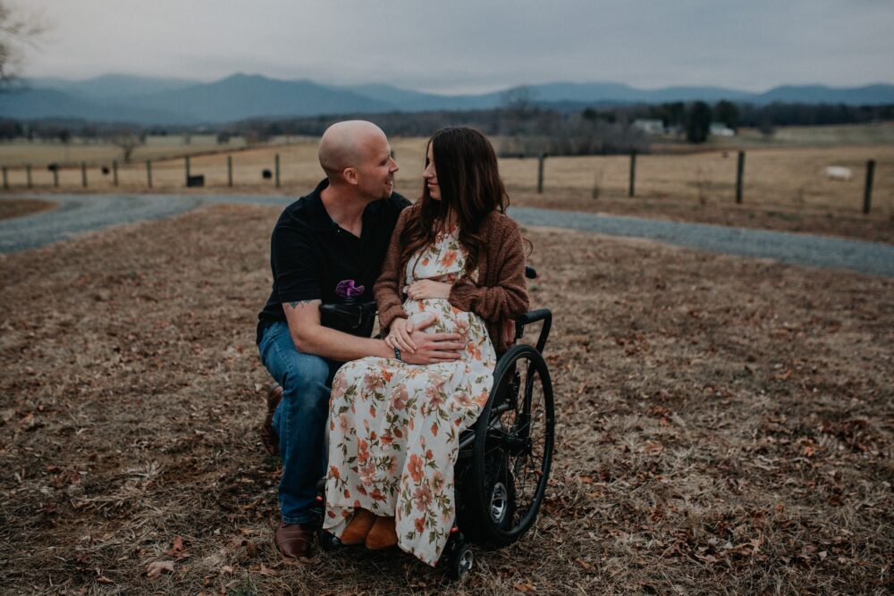 Pregnant woman in wheelchair with partner, mountain backdrop. Dani's Twins journey.