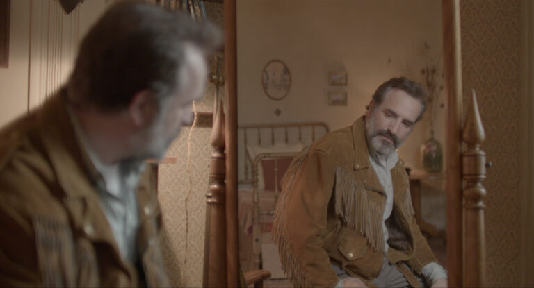 Man in a fringed jacket looking in a mirror.