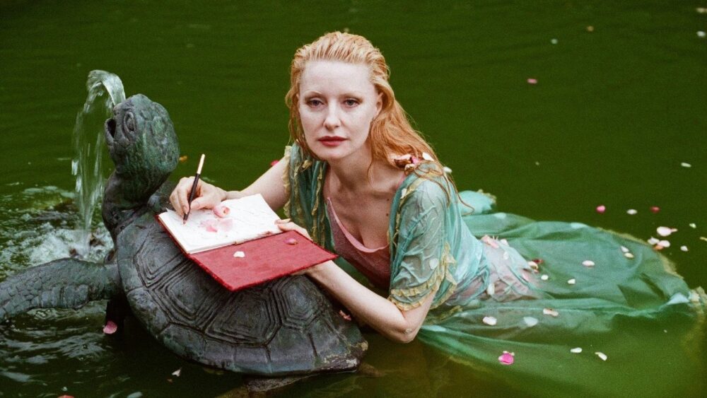 Woman in water with turtle statue, holding a notebook and pen.
