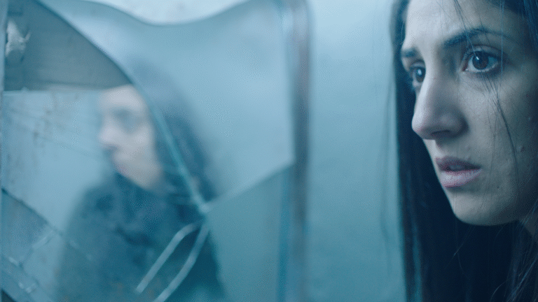 Woman's reflection in cracked glass, conveying a sense of mystery or horror, possibly related to "Dachra.