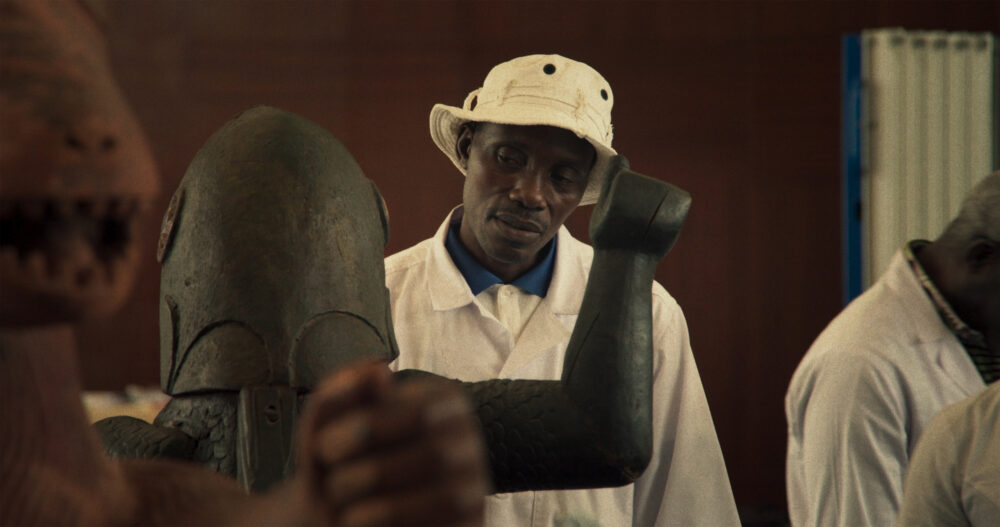 Man in white coat with Dahomey art statue