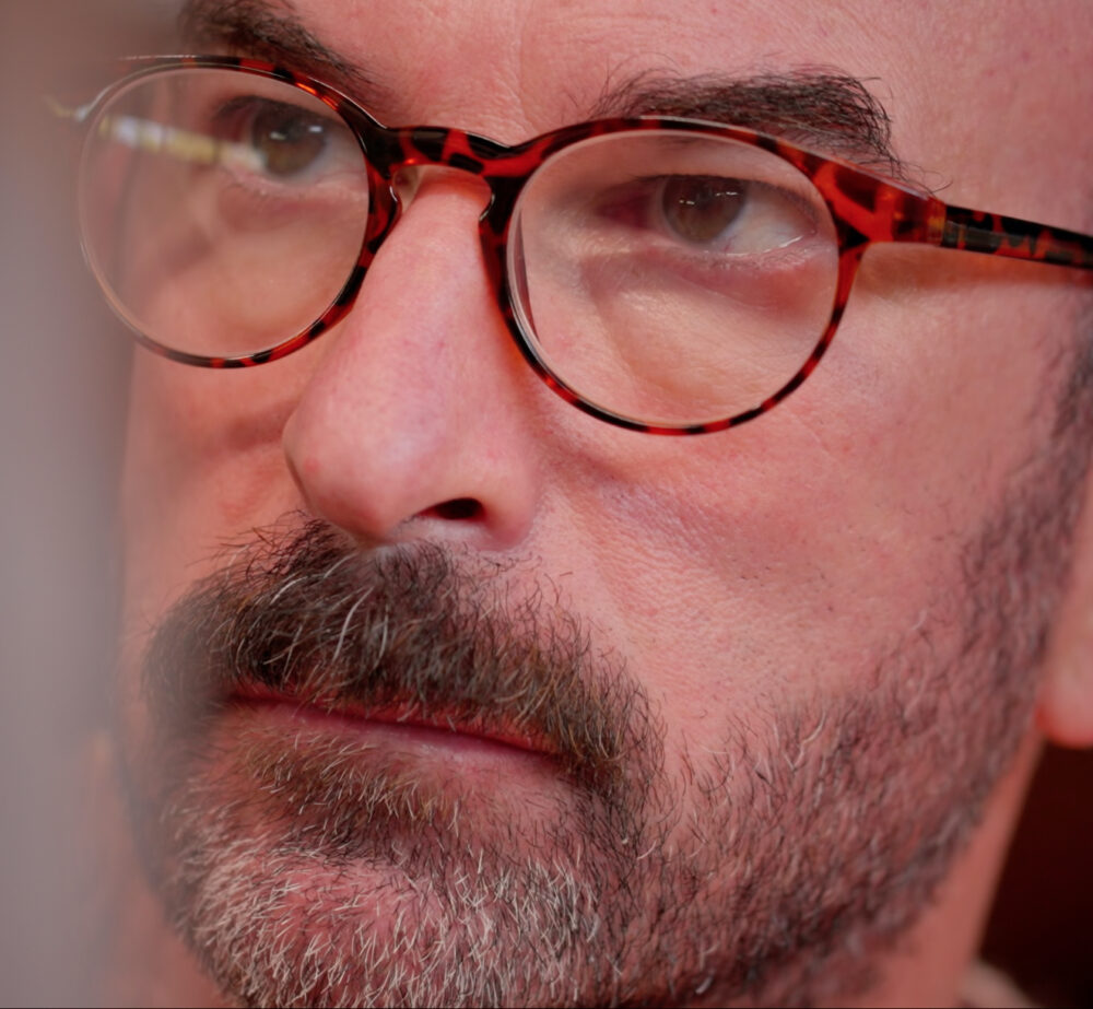 Close-up of Daniel Freed with glasses and a beard, looking to the side.