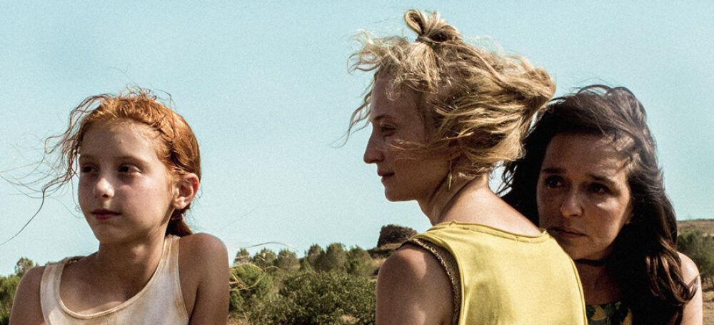Three women stand together in a sunlit field. "Daughter of Mine" movie image.