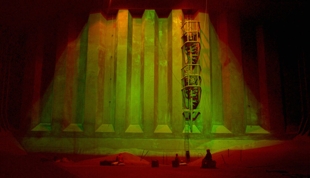 Ship's hold with workers, ladder, and green lighting. "Dead Slow Ahead" could describe the slow work pace.