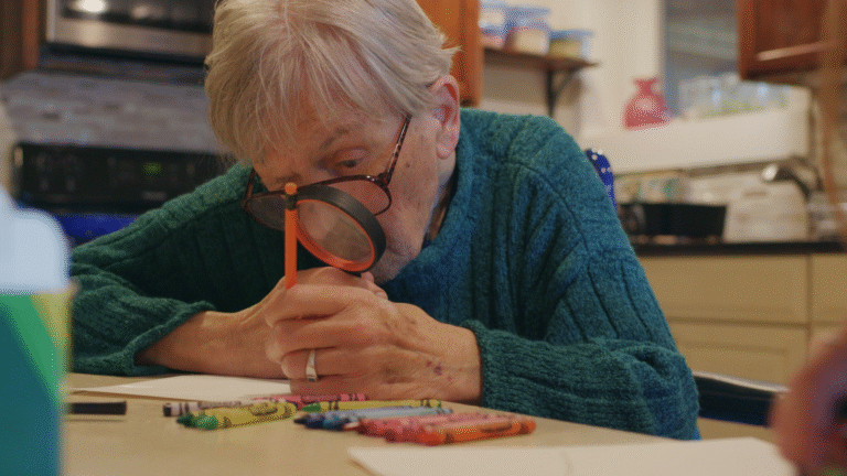 Senior man with dementia using magnifier and crayons, focusing on art. Living well with dementia.
