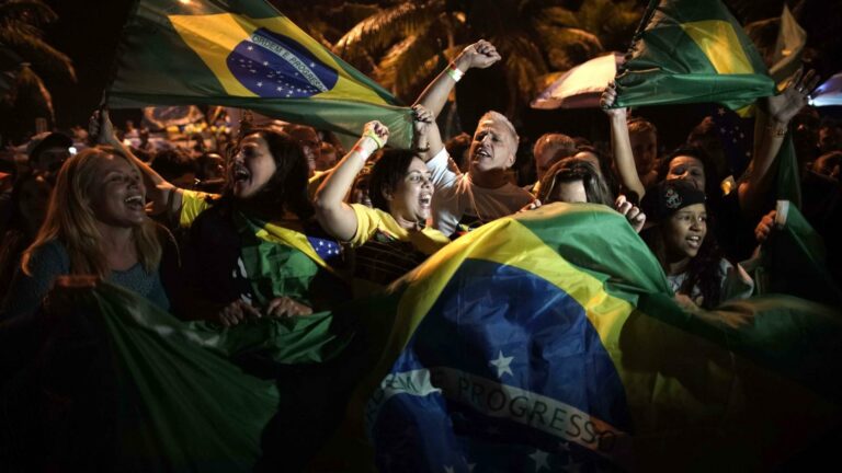 Crowd celebrating, waving Brazilian flags, possibly related to dismantling democracy discussions.