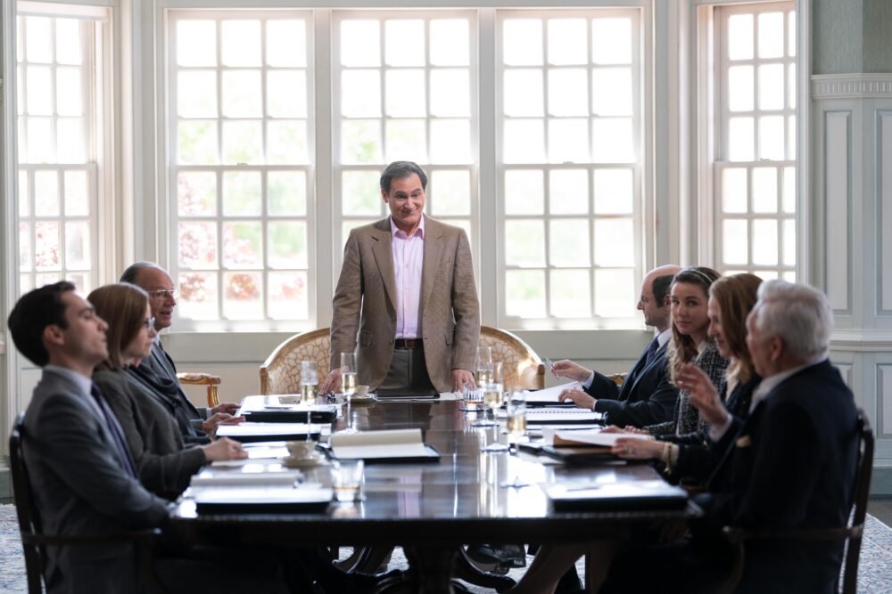 Meeting scene from "Dopesick": man standing at a table with seated colleagues.