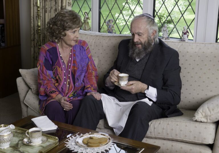 Elderly couple on sofa, man with kippah holds tea.