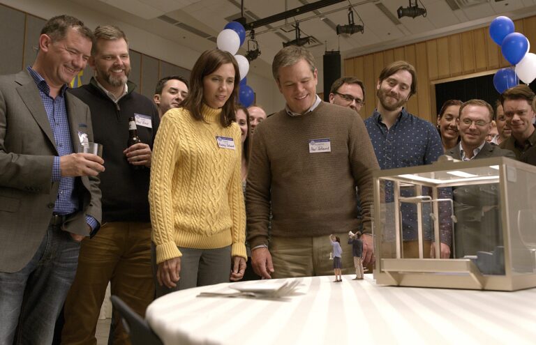 Matt Damon and Kristen Wiig in "Downsizing" looking at a model of a tiny house with other people.