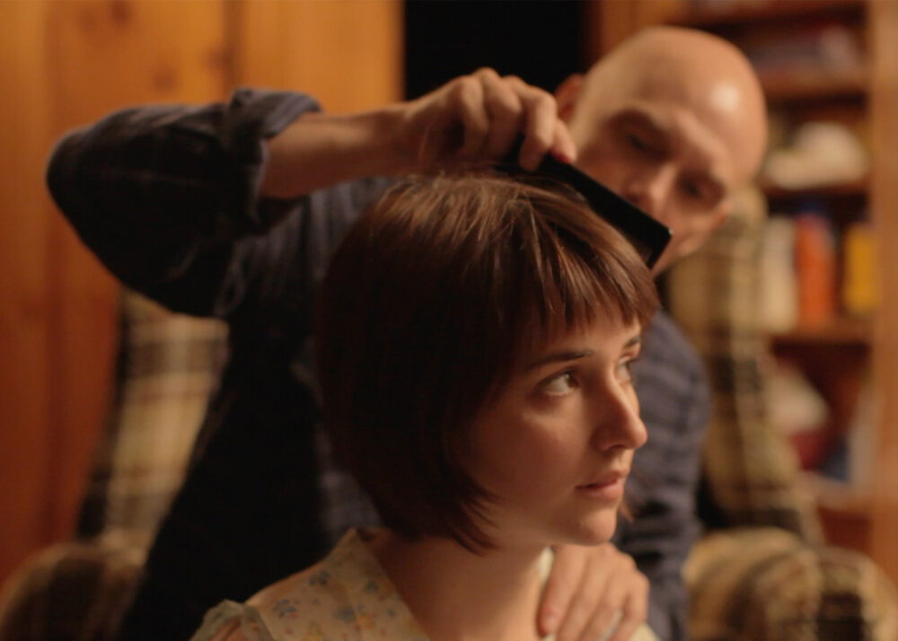 Bald man combing a woman's short brown hair.