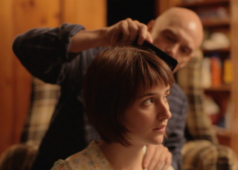 Bald man combing a woman's short brown hair.