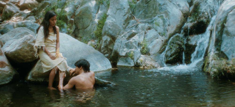 Couple by a waterfall: Woman sitting on a rock, man in the water.